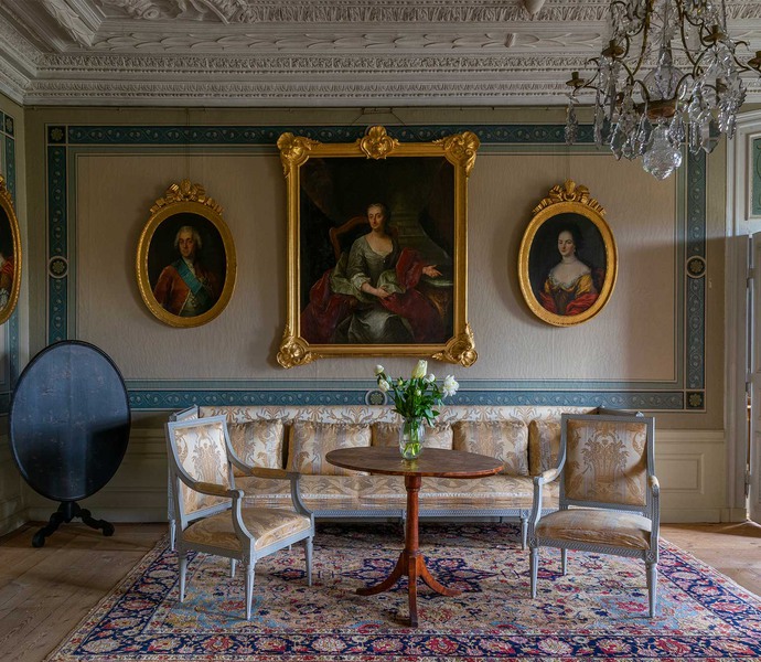Ett slottsrum i beige och blått med flertalet stora porträtt.