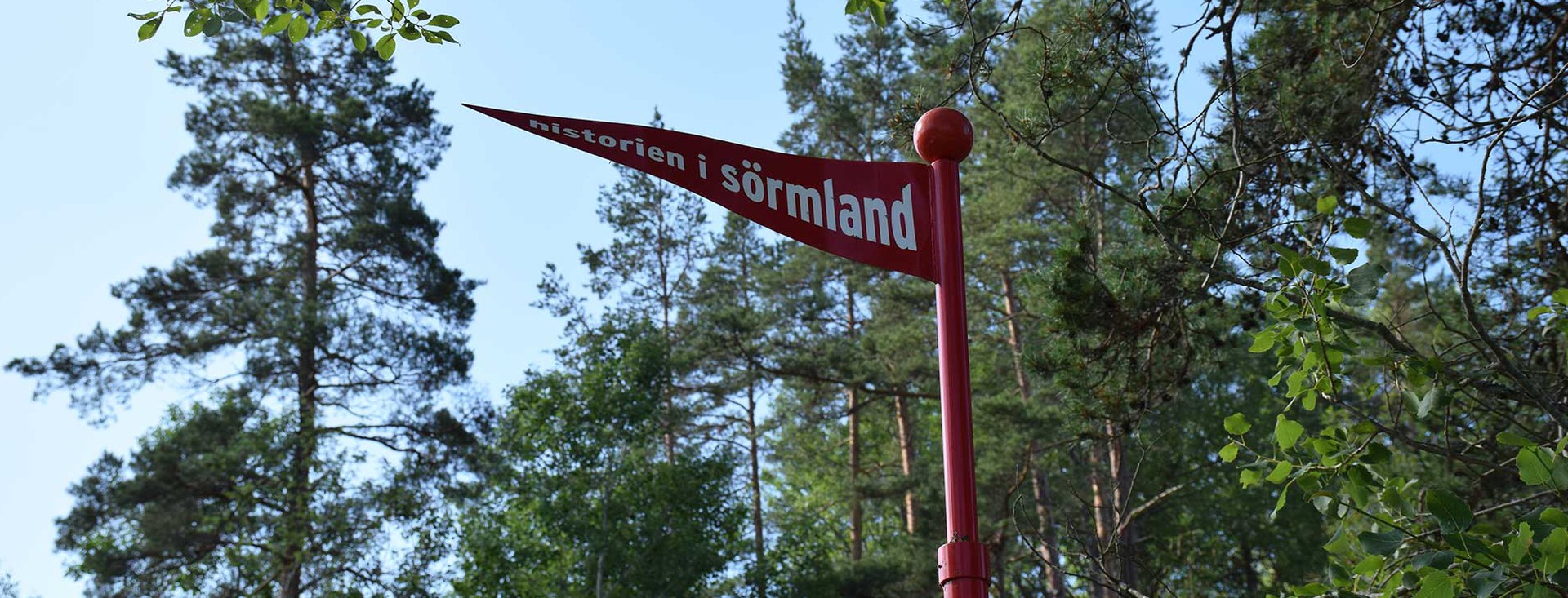 En röd metallflagga med texten "Historien i Sörmland"