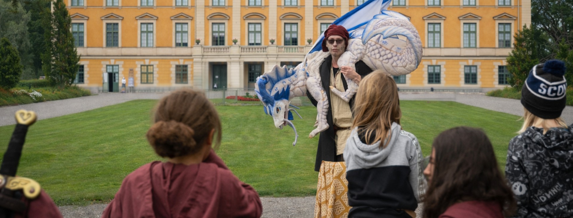 Utklädd person går framför Nynäs slott med en drake på sina axlar.